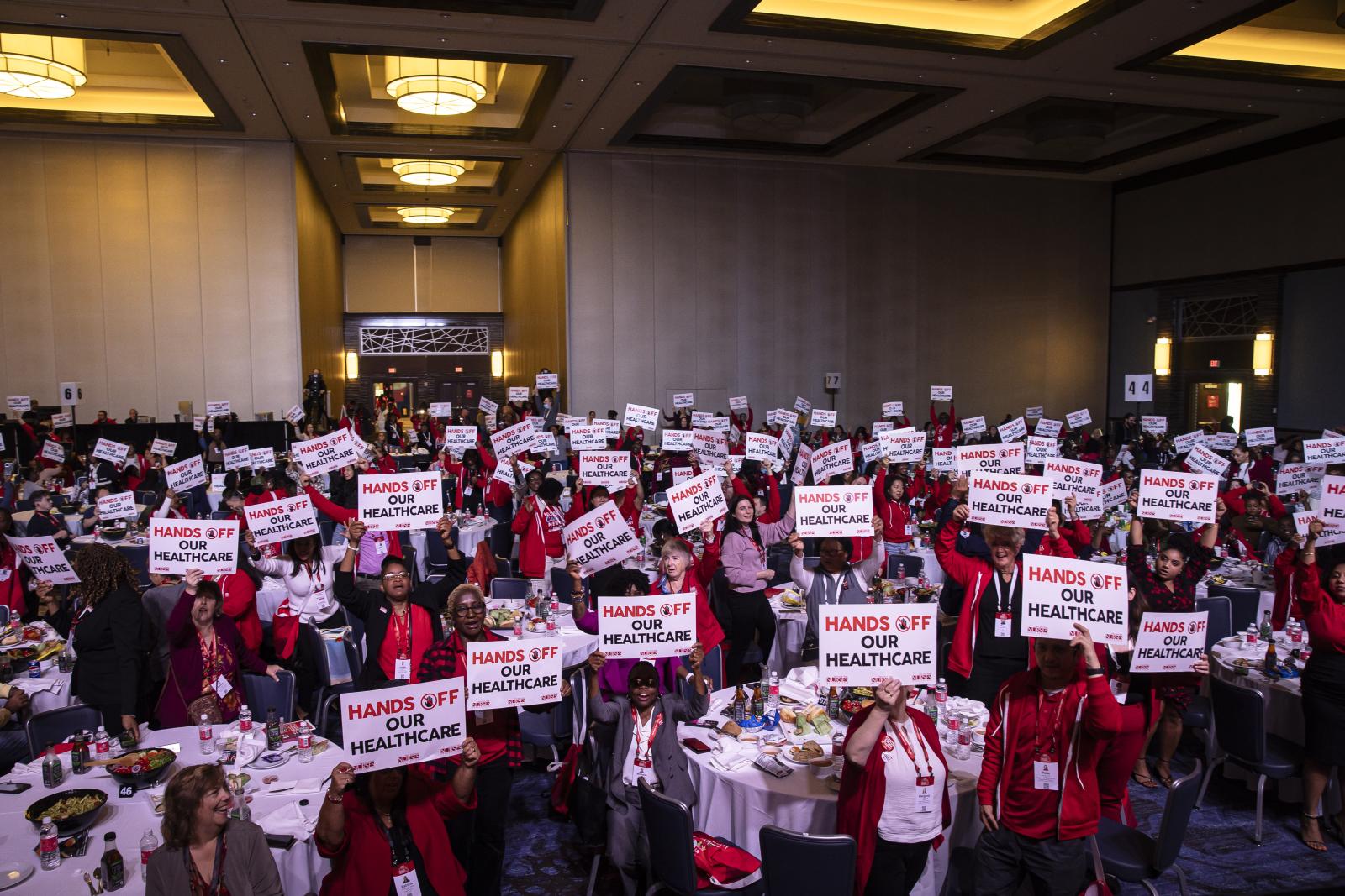 Large group of nurses holding signs that say "hands off our healthcare"