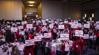 Large group of nurses holding signs that say "hands off our healthcare"