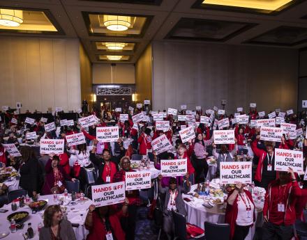 Large group of nurses holding signs that say "hands off our healthcare"
